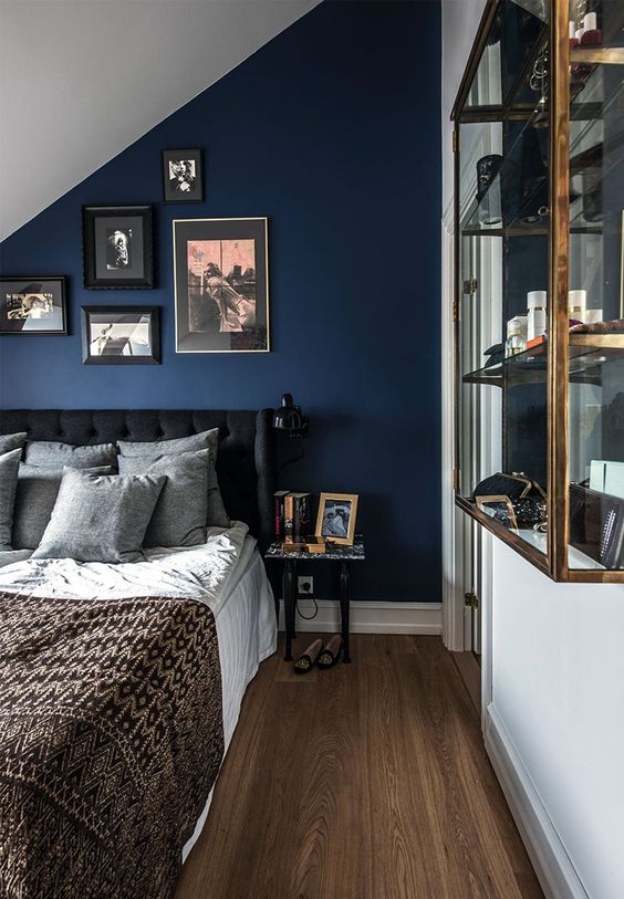 an elegant attic bedroom with a navy accent wall, a black bed, a gallery wall, a glass storage unit is chic