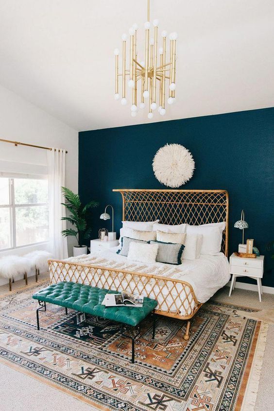 an elegant bedroom with a teal wall, a woven bed, a turquoise bench, a gold chandelier and a boho rug