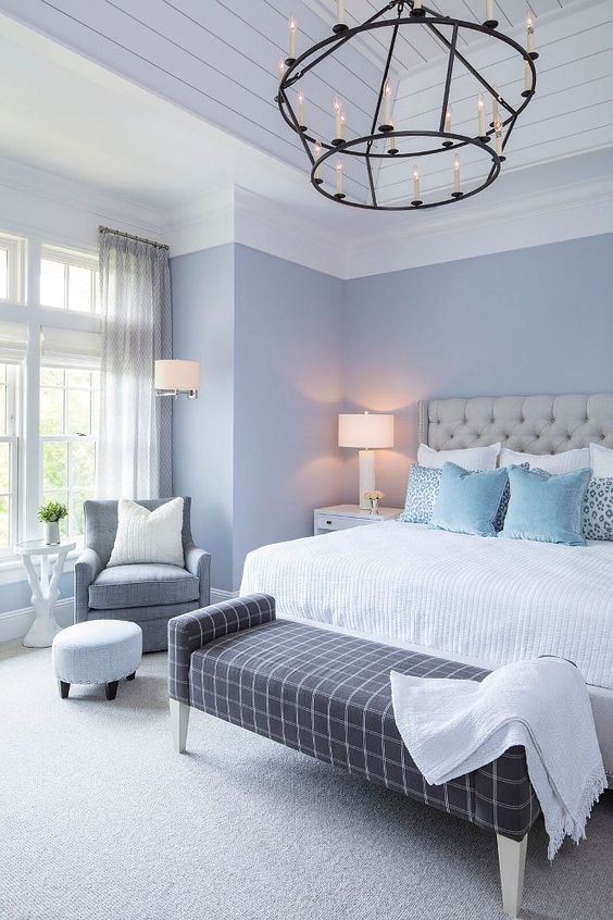 an elegant bedroom with light blue walls, a grey leather bed, a windowpane print bench, a vintage chandelier and greys here and there