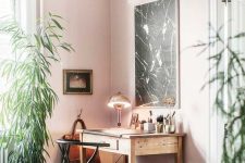 an elegant home office with light pink walls, a vintage desk and chair, a black marble artwork and a statement plant