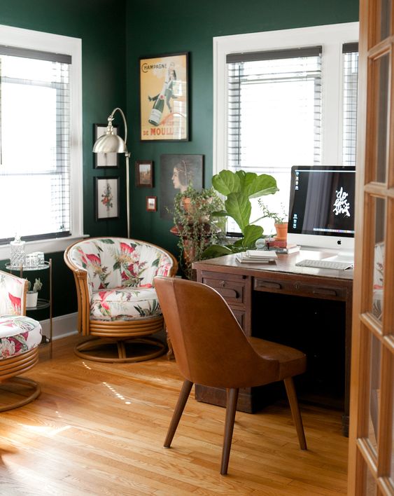 an elegant mid-century modern home office with hunter green walls, dark stained furniture, a leather chair, a gallery wall and a potted plant