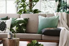 an elegant tropical living room in neutrals, with a grey sofa, stumps, potted plants and tropical pillows
