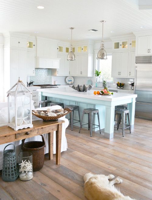 an enchanting coastal kitchen with white cabinets, a light blue kitchen island and a matching backsplash, shiny pendant lamps