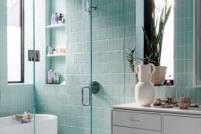 an ethereal aqua blue bathroom clad with skinny tiles, with built-in shelves, a floating vanity and a fun rug