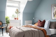 an ethereal attic bedroom with light blue walls, jewel tone bedding, a rattan chair and some potted plants
