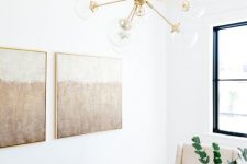 an ethereal neutral home office with a wooden desk, neutral chairs, a chic gallery wall, a gold chandelier and greenery