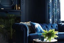 an exquisite living room with midnight blue walls, a navy sofa and floral curtains, greenery and brass touches