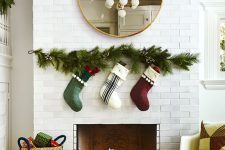 a Christmas fireplace with candle lanterns and lights, evergreens and stockings over the fireplace and a basket with gifts