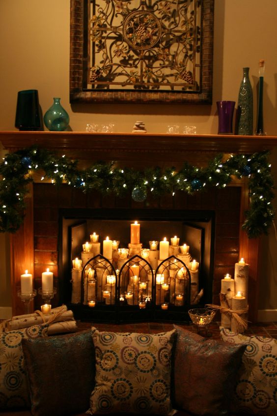 a Christmassy fireplace with evergreens, lights, pillar candles inside and a lovely screen is very cozy