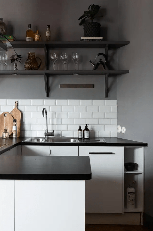 a Scandinavian kitchen with grey walls, white lower cabinets, black countertops, soot shelves and white subway tiles