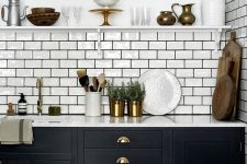 a bold black kitchen with a white subway tile backsplash accented with black grout and touches of gold and brass