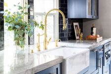 a bold blue kitchen with a black subway tile backsplash, white marble countertops and lots of gold for a shiny feel