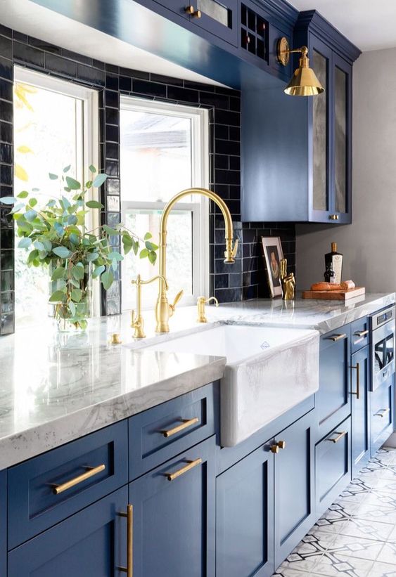 a bold blue kitchen with a black subway tile backsplash, white marble countertops and lots of gold for a shiny feel