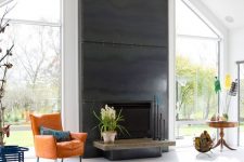 a bold light-filled living room with a fireplace clad with blackened steel sheets and with a bright leather chair in front of it