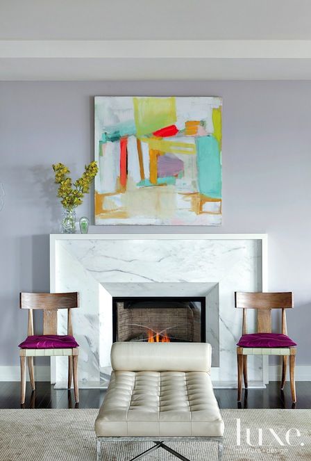 a bold refined nook with a white marble fireplace, fuchsia chairs, a bright artwork and a white leather bench