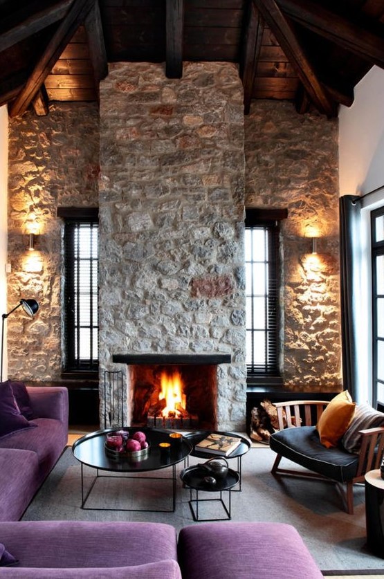 a bright contemporary living room with rough stone walls and a fireplace, purple furniture and elegant round tables