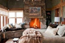 a cabin bedroom with a rough stone fireplace and a bench, a catchy chandelier, wooden items and a cozy linens