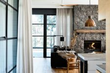 a chalet living room with a rough stone fireplace, black upholstered and wooden furniture and a metal pendant lamp