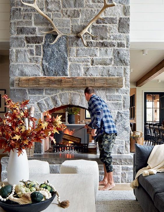 a chalet living room with a stone fireplace, a coffee table and neutral stools, some lovely fall decor