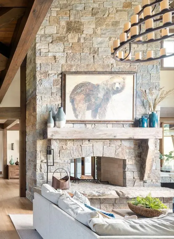 a chalet living room with a stone fireplace, a white sectional, some pretty decor and a gorgeous tiered chandelier