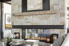 a chalet living room with stone stools, a low marble coffee table and seating furniture plus an amazing double-sided stone fireplace