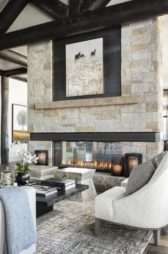 A chalet living room with stone stools, a low marble coffee table and seating furniture plus an amazing double sided stone fireplace