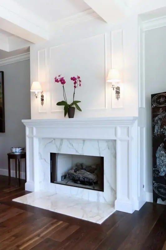 a chic and stylish marble fireplace with some marble on the floor and a vintage white mantel over it is refined