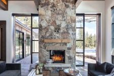 a chic contemporary cabin space with dark furniture, wood slab tables and a spectacular stone fireplace with a wooden mantel