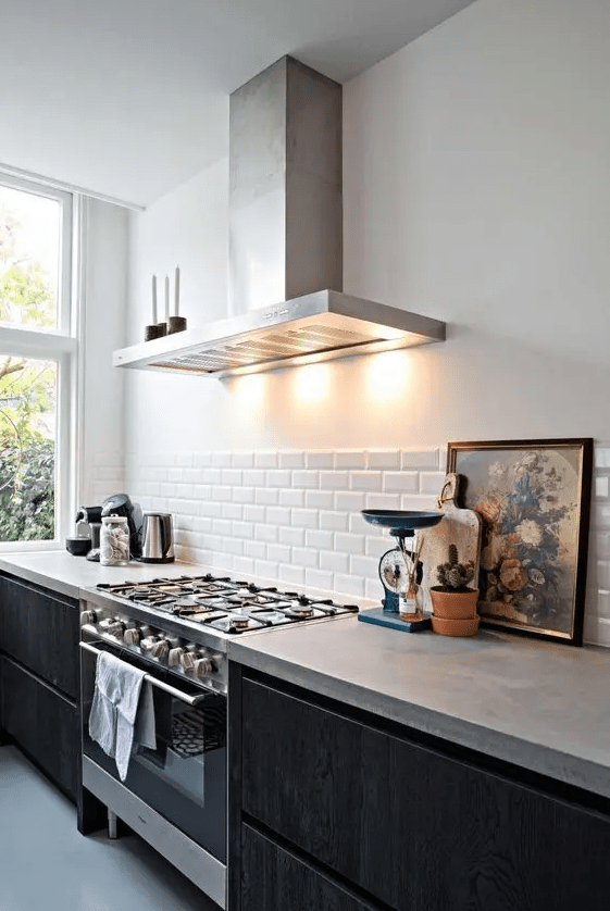 a chic contemporary kitchen with black lower cabinets and concrete countertops,a white subway tile backsplash and some decor