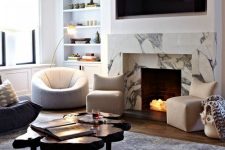 a chic modern living room in neutrals, with a faux fireplace clad with white marble and lit up firewood inside it