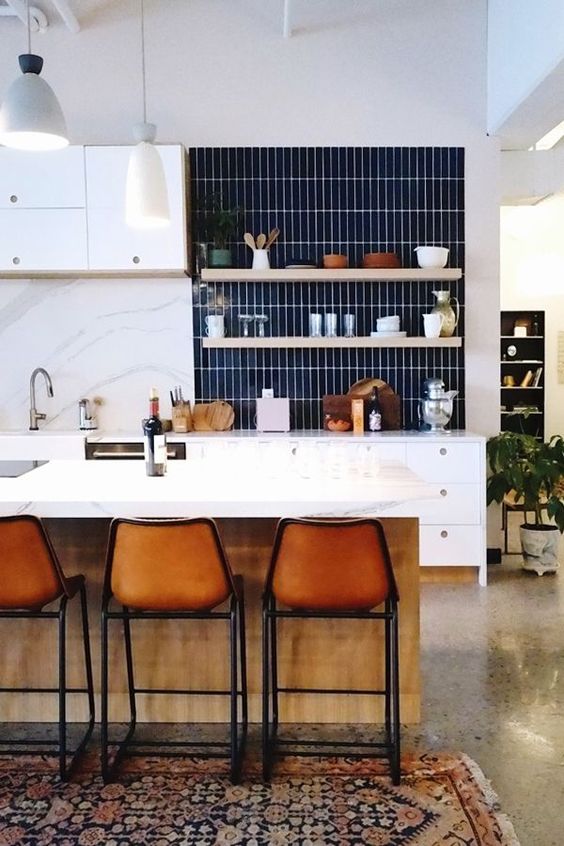 a chic modern white kitchen with a navy stacked tile backsplash and borwn leather stools