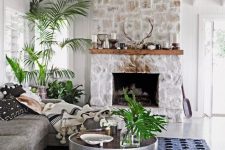 a chic monochromatic living room with a whitewashed stone fireplace, a wooden mantel with candles and antlers and potted plants