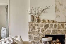 a chic neutral living room with a rough stone fireplace and neutral furniture, blooming branches that brings warmth here