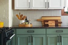 a chic two-tone kitchen in green and white, with a grey penny tile backsplash and a black stone countertop
