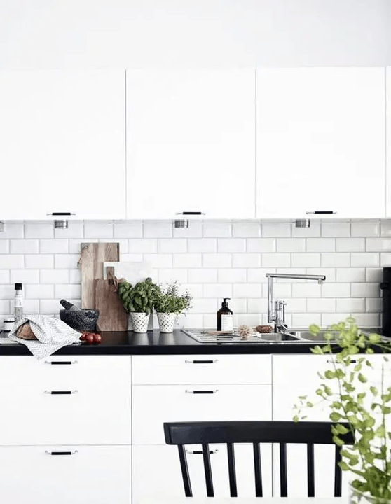 a classic white Scandinavian kitchen with black countertops, a white subway tile backsplash and black handles