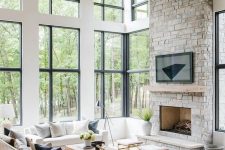a clean and modern double-height living room with a grey stone fireplace and a wooden mantel as a centerpiece