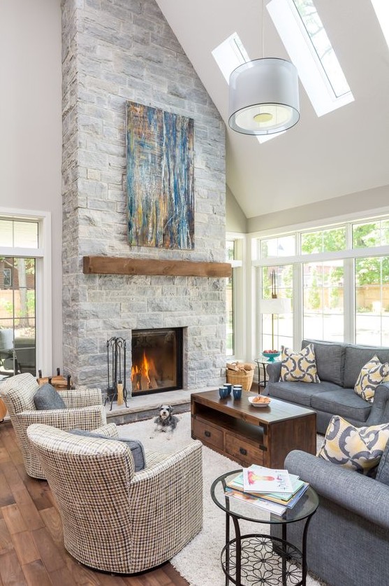 A clean double height neutral living room with a grey stone fireplace with a wooden mantel and a bright blue artwork
