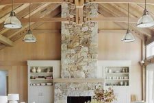 a coastal barn living room with a stone fireplace, neutral furniture and pendant lamps plus potted plants