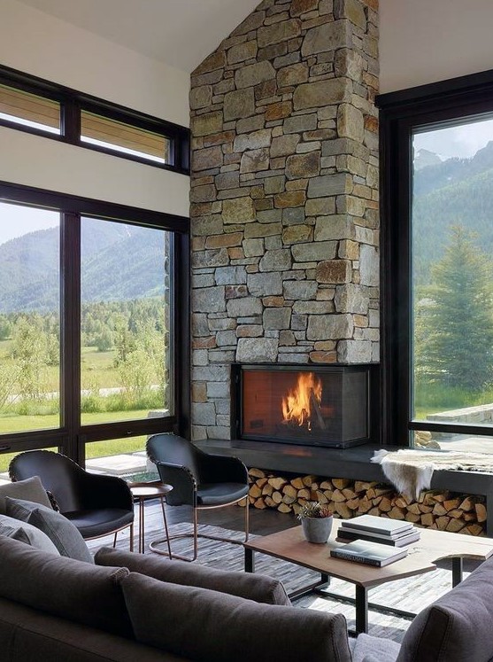 a contemporary cabin living room with a stone clad fireplace and firewood storage, chic furniture and lots of windows