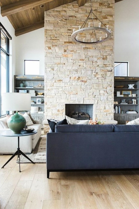 a contemporary living room in neutrals, with a double-height ceiling, a stone fireplace that warms up the space