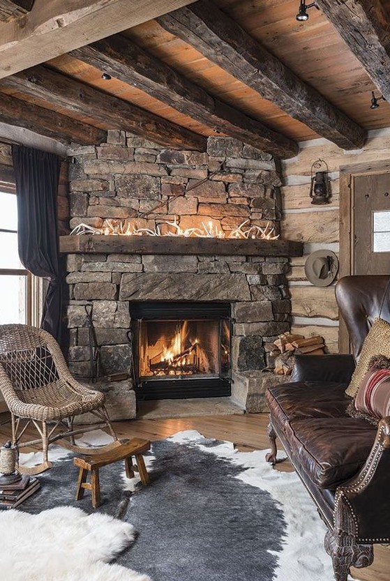 a dak cabin living room with a stone fireplace, antlers on the mantel, layered rugs and wicker and leather furniture
