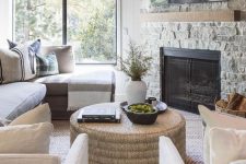 a farmhouse living room with a stone fireplace, a grey sofa, white chairs, a black side table and jute coffee table