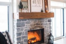 a farmhouse living room with a stone fireplace, a mantel with winter decor and a plaid chair feels and looks very cozy