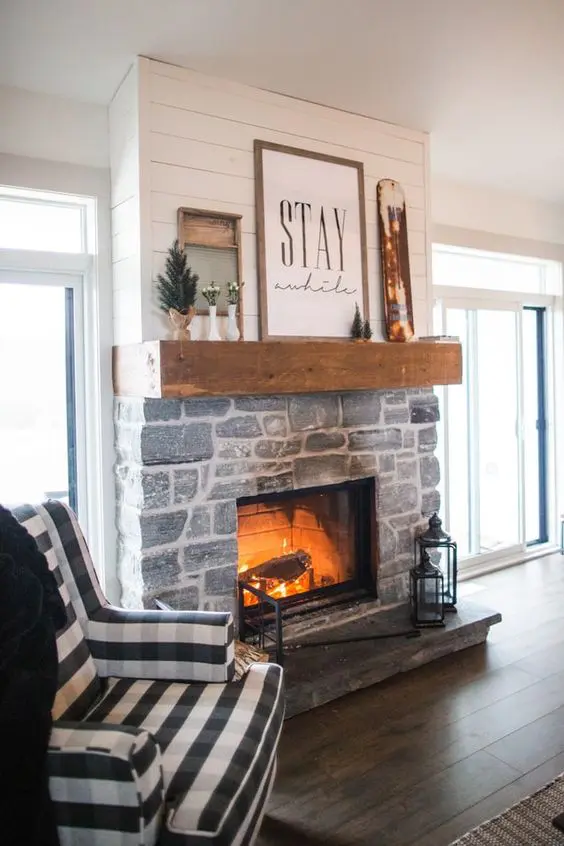 a farmhouse living room with a stone fireplace, a mantel with winter decor and a plaid chair feels and looks very cozy