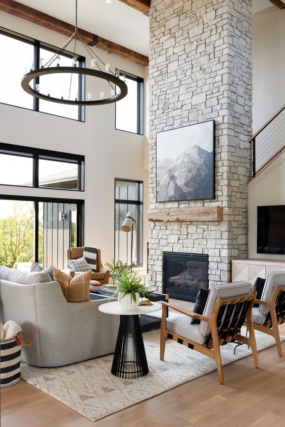 a farmhouse living room with a stone fireplace, neutral seating furniture, chairs, coffee tables and a chandelier
