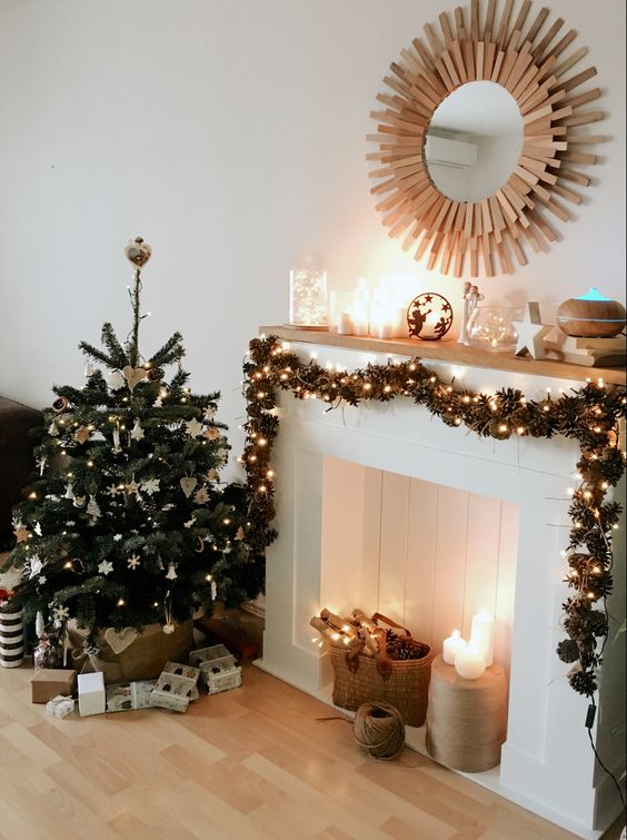a faux fireplace with pinecones and lights, pillar candles, a pinecone and light garland and candles on the mantel