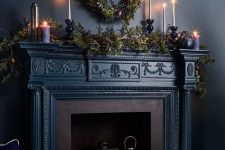 a gorgeous dark fireplace with candle lanterns and candleholders, evergreens and candles on the mantel