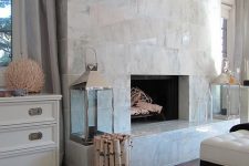 a large non-working fireplace clad with white marble tiles all over, with candle lanterns and firewood in a vase
