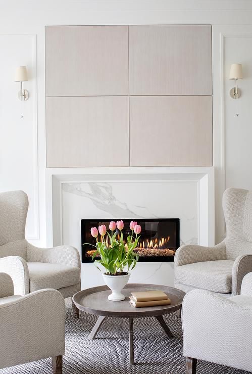 a light-filled neutral and pastel living room with a marble clad fireplace and a cool sitting zone by its side