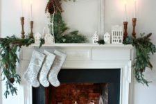 a lovely Christmas fireplace with pillar candles and candle lanterns, a basket with firewood, evergreens and tall and thin candles
